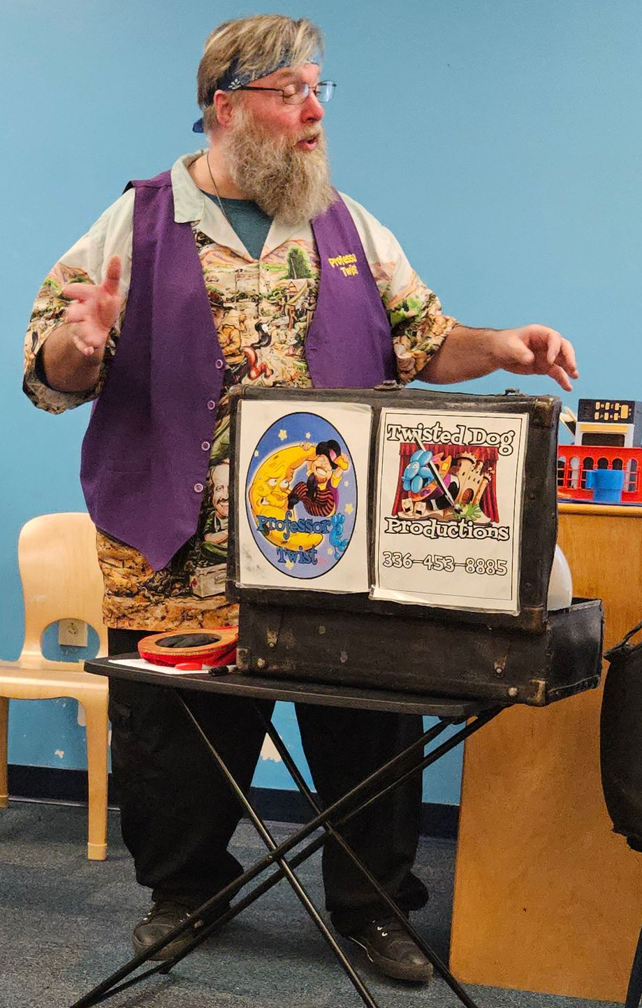 Magician performing on stage at a mall, surrounded by children and adults.
