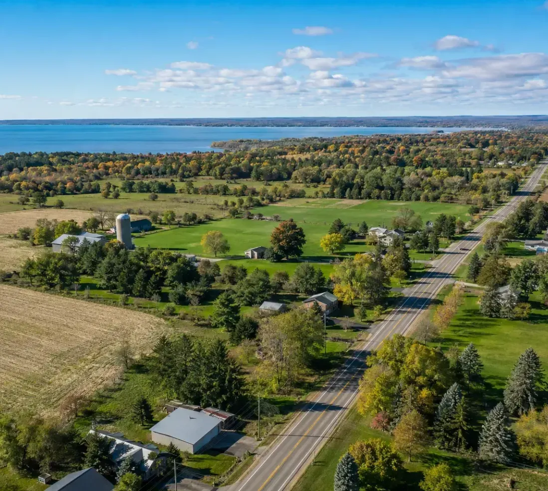 Aerial view of rural farmland, scattered homes, and a road leading toward a lake under a blue sky