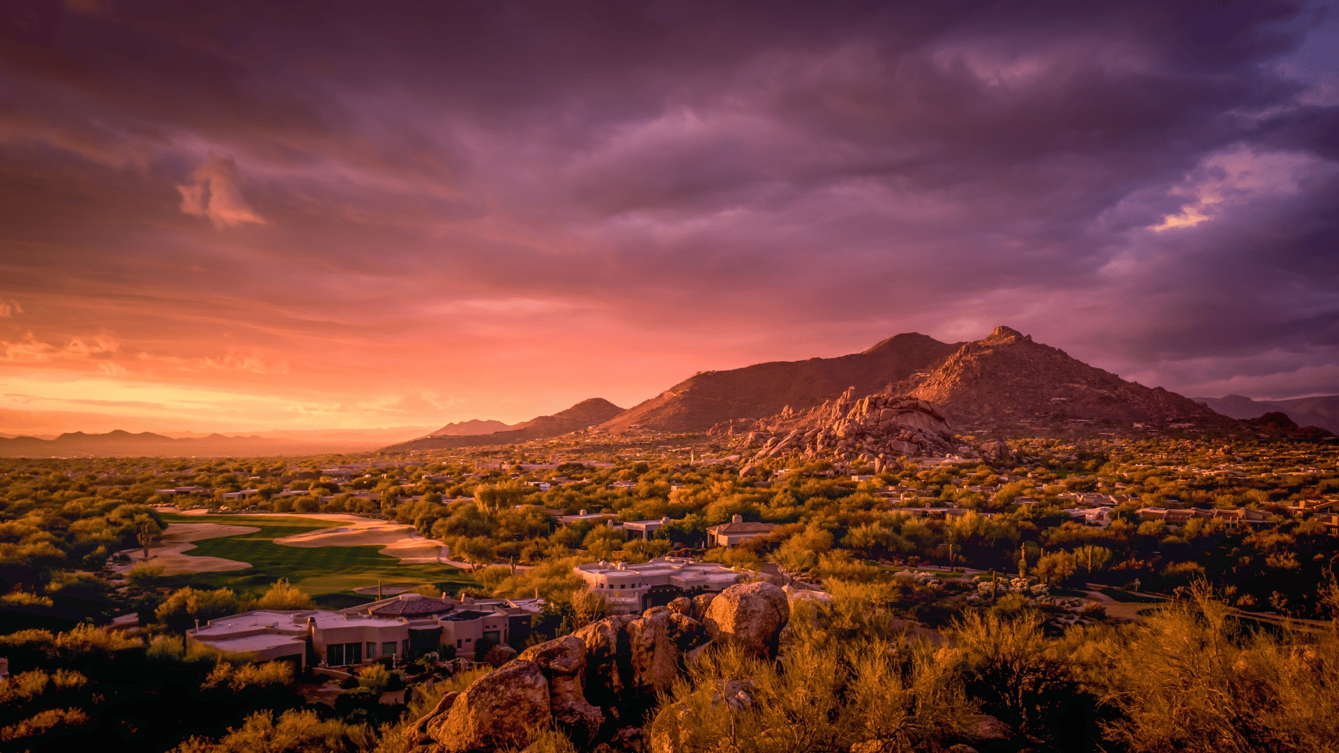An aerial view of a desert landscape at sunset with mountains in the background.