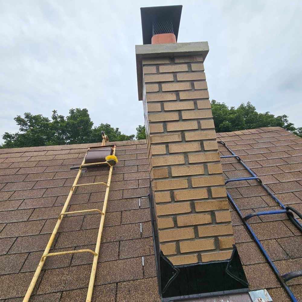 Roof with brick chimney and two ladders leaning on shingles under a cloudy sky