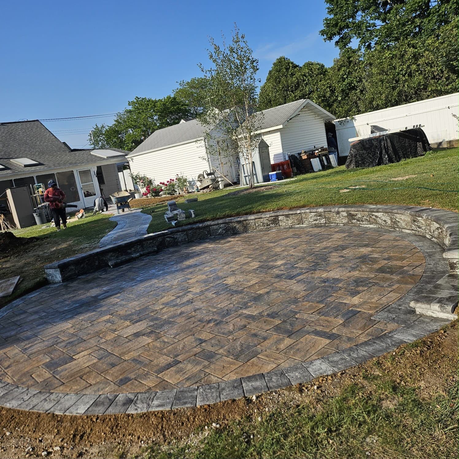 Backyard with a circular brick patio and small fountain, surrounded by grass and suburban houses