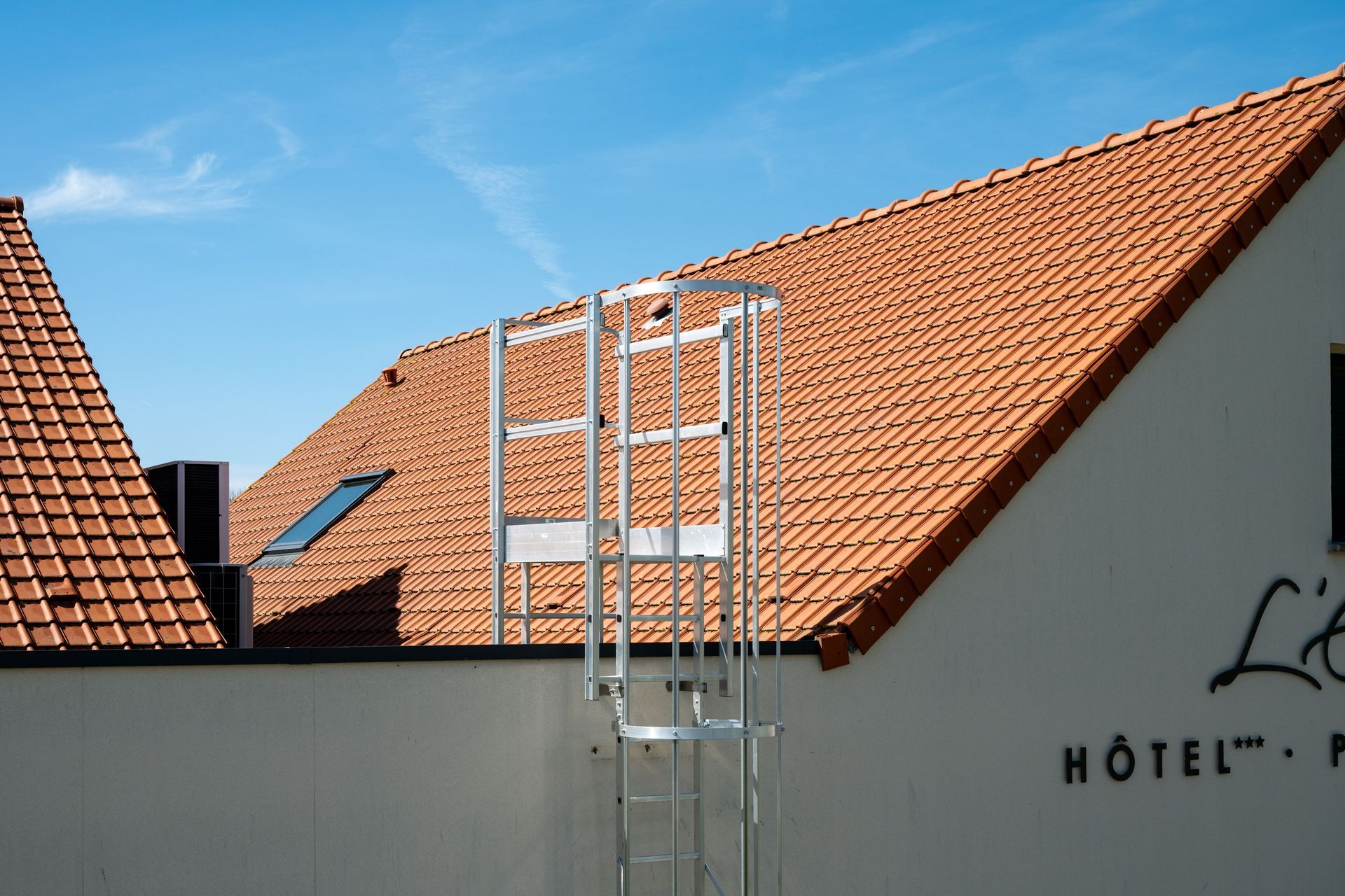 Red-tiled rooftops and a white hotel wall with a metal ladder against a blue sky