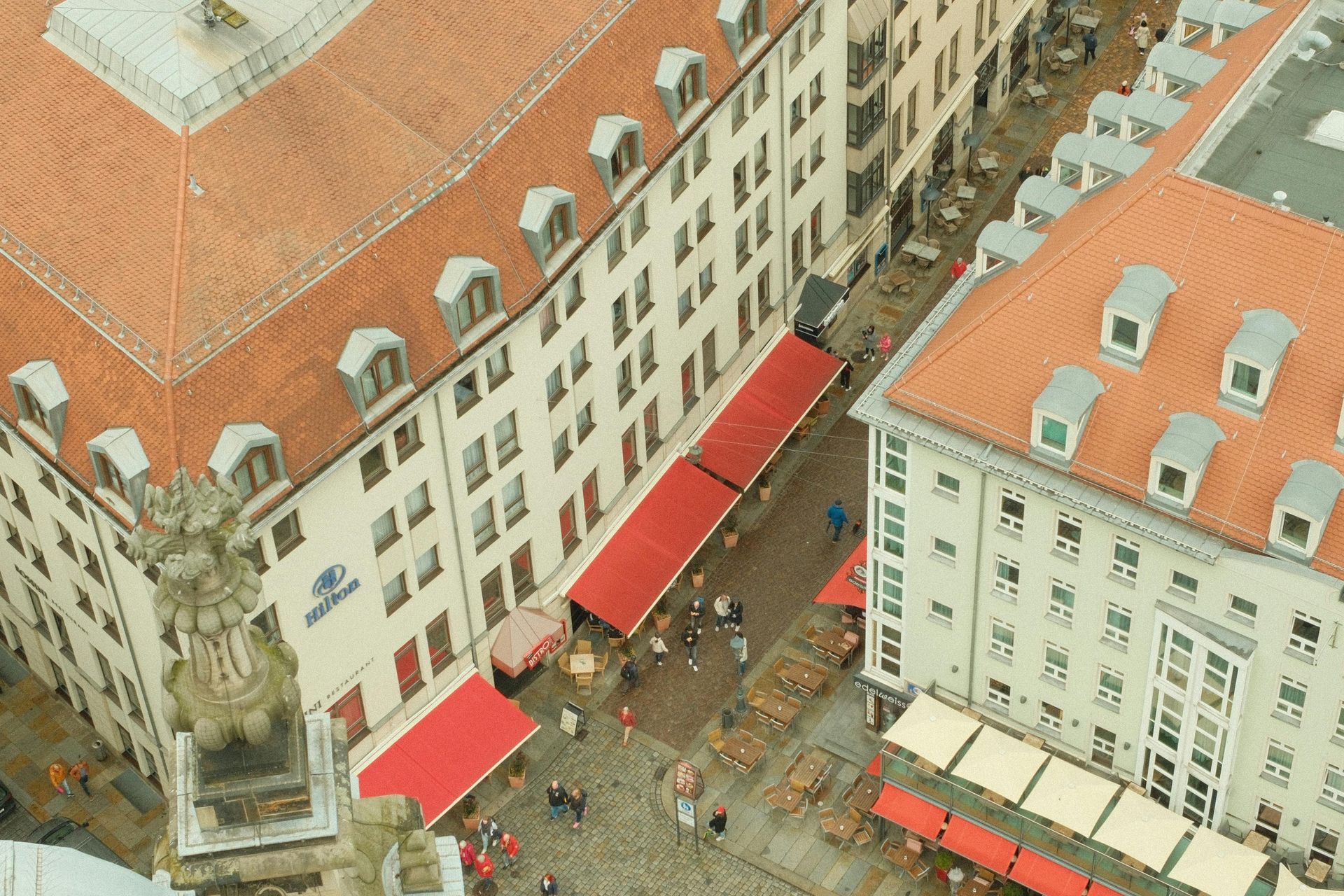 Aerial view of a narrow street lined with white buildings and red roofs, with outdoor market stalls below