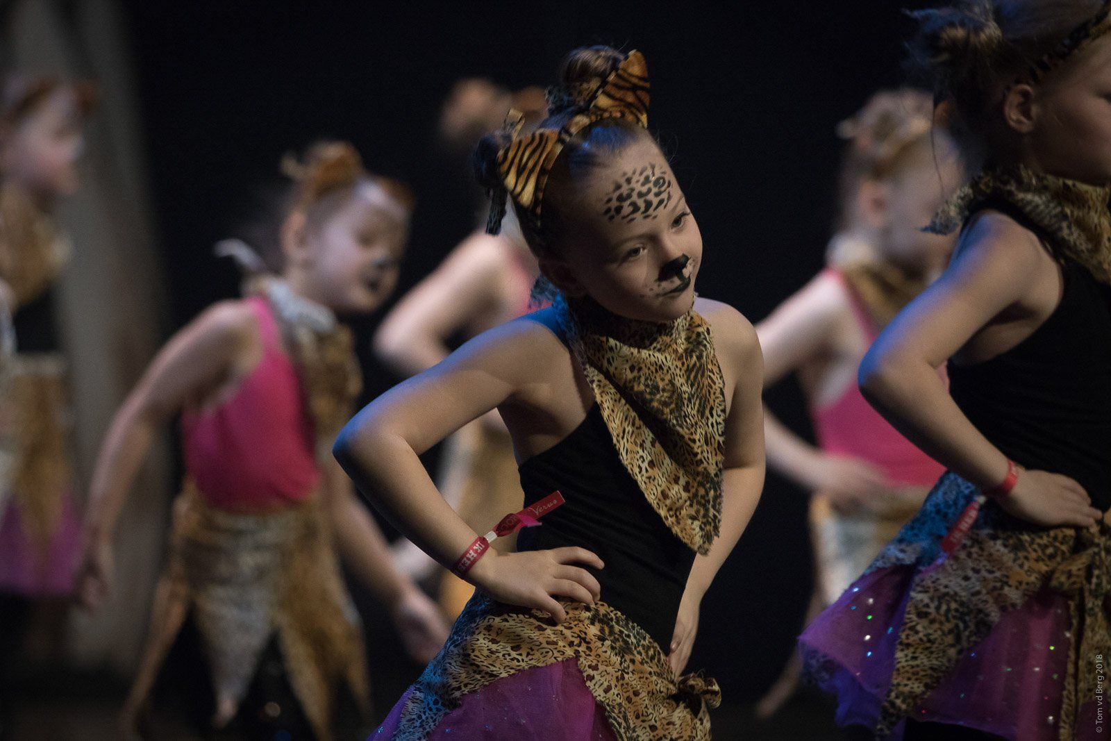 Kinderen in luipaardkostuums dansen op het podium, met hun handen in hun zij en geschminkte gezichten.