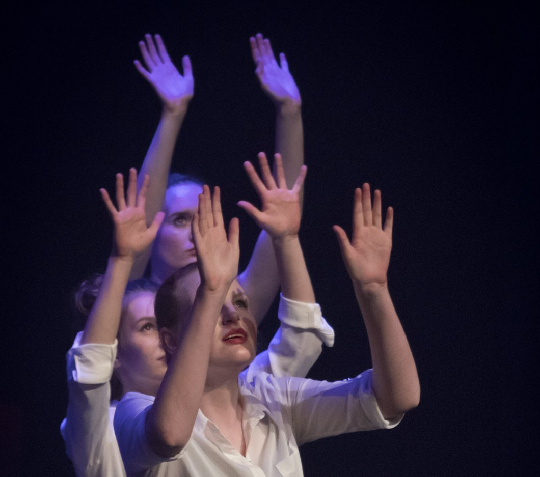 Vier dansers in witte shirts met hun handen omhoog.