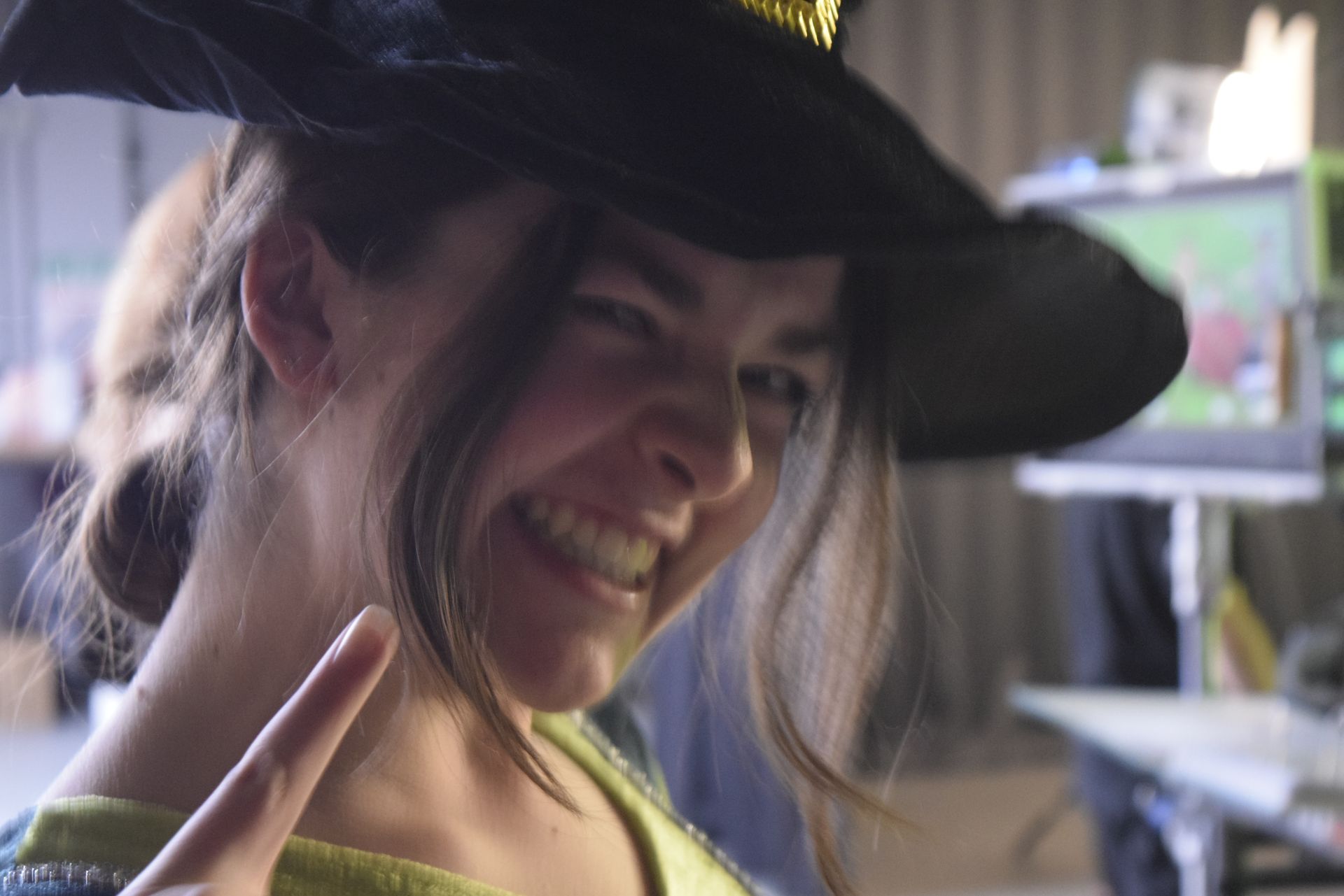 Vrouw met een zwarte heksenhoed die knipoogt, lacht en een vredesteken maakt.