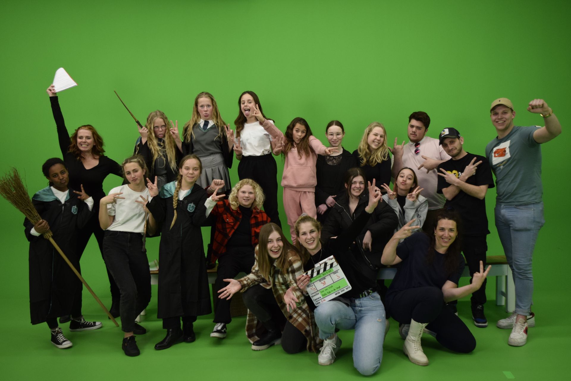 Een groep mensen poseert voor een groen scherm, sommigen houden rekwisieten vast zoals een toverstaf of een script.