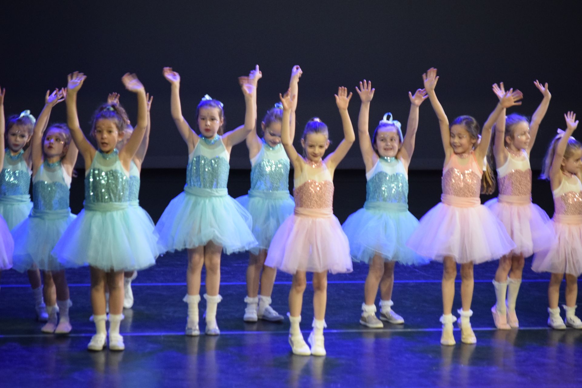 Jonge danseressen in tutu's en glinsterende topjes met hun armen omhoog op het podium.