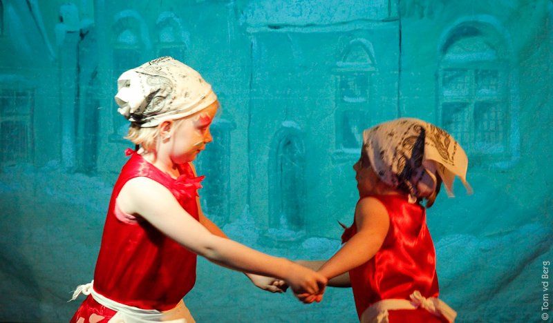 Twee kinderen in rode outfits en met hoofddoeken dansen hand in hand op het podium.