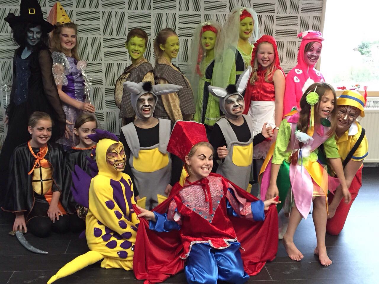 Een groep verklede kinderen poseert; verschillende personages zoals een heks en dieren met kleurrijke make-up.