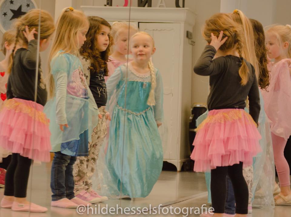 Kinderen in tutu's en kostuums in een dansstudio, voor een spiegel. Een van de meisjes draagt ​​een Elsa-jurk.
