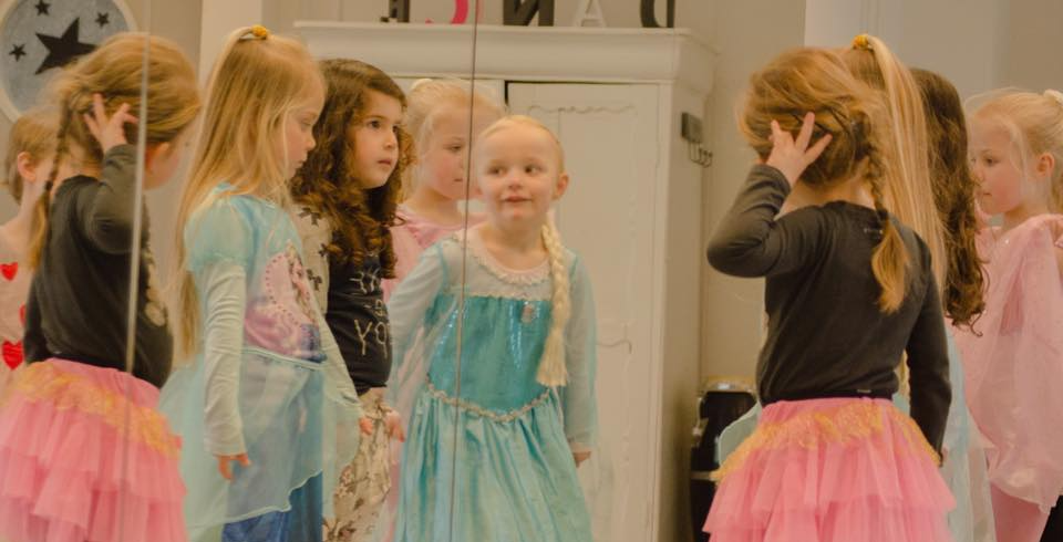 Meisjes in dansles, sommigen in prinsessenkostuums, kijken in een spiegel.