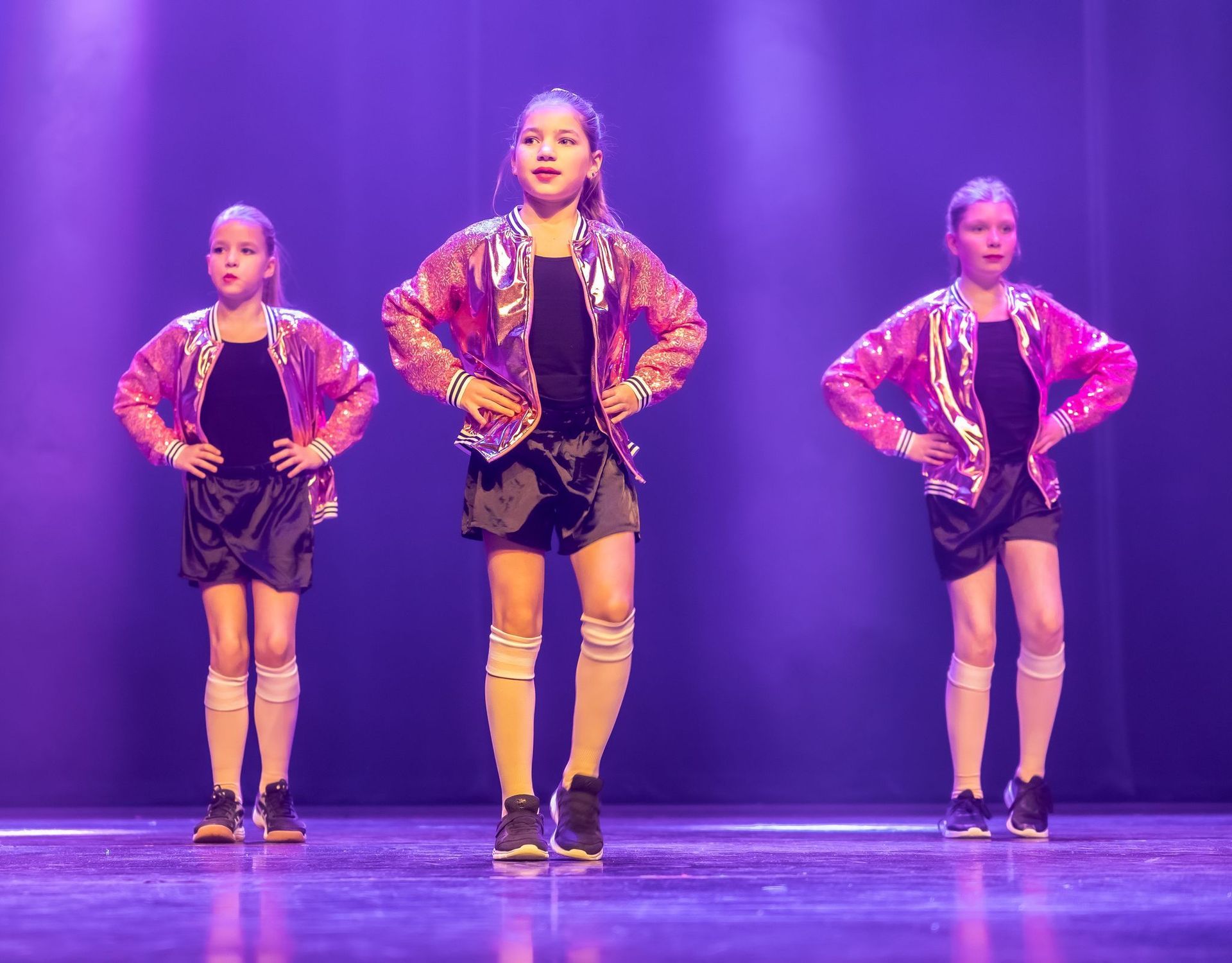 Drie dansers in glanzende jasjes en korte broeken staan ​​op het podium, met hun handen in hun zij.