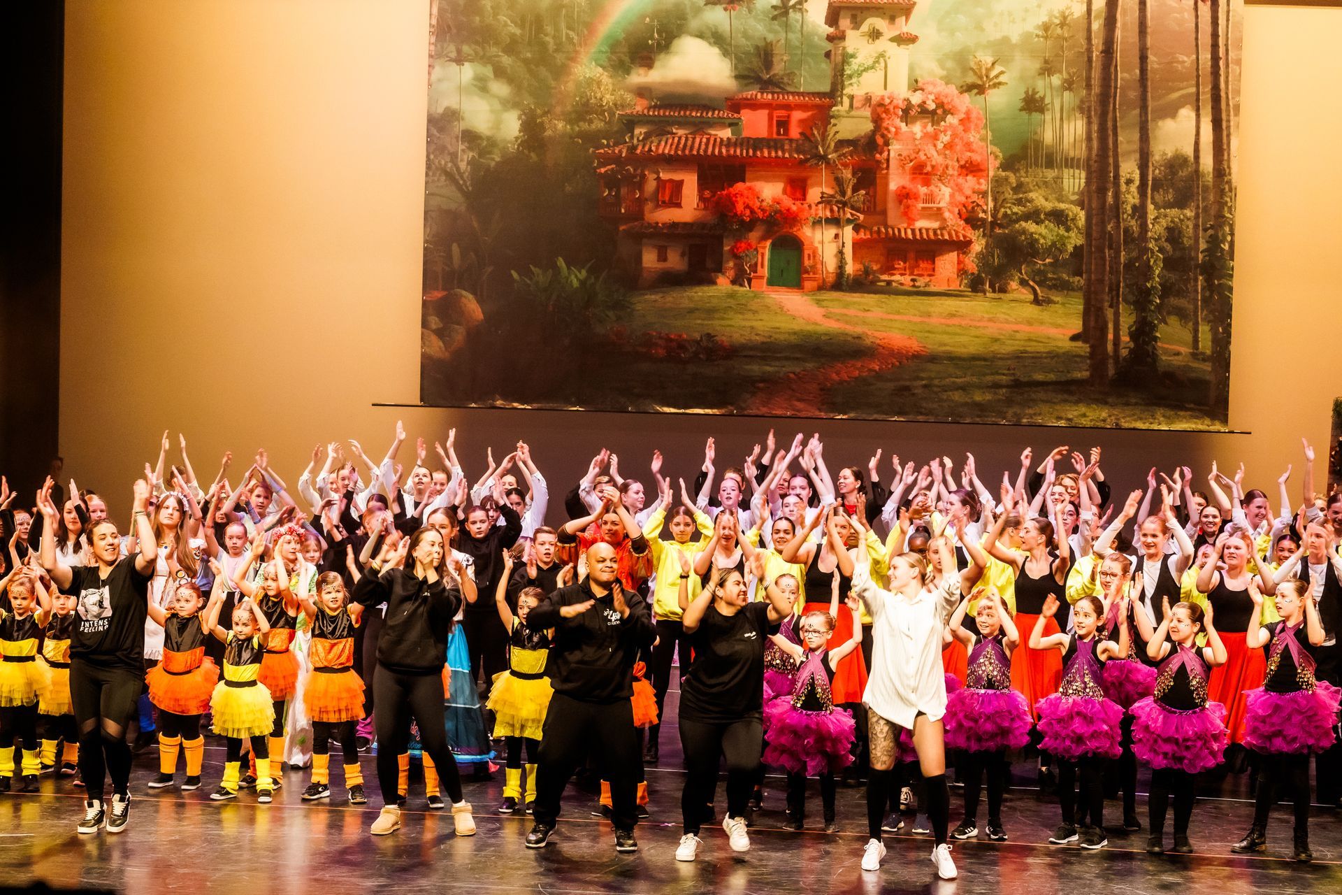 Een grote groep dansers staat op het podium op de achtergrond decor van encanto show.