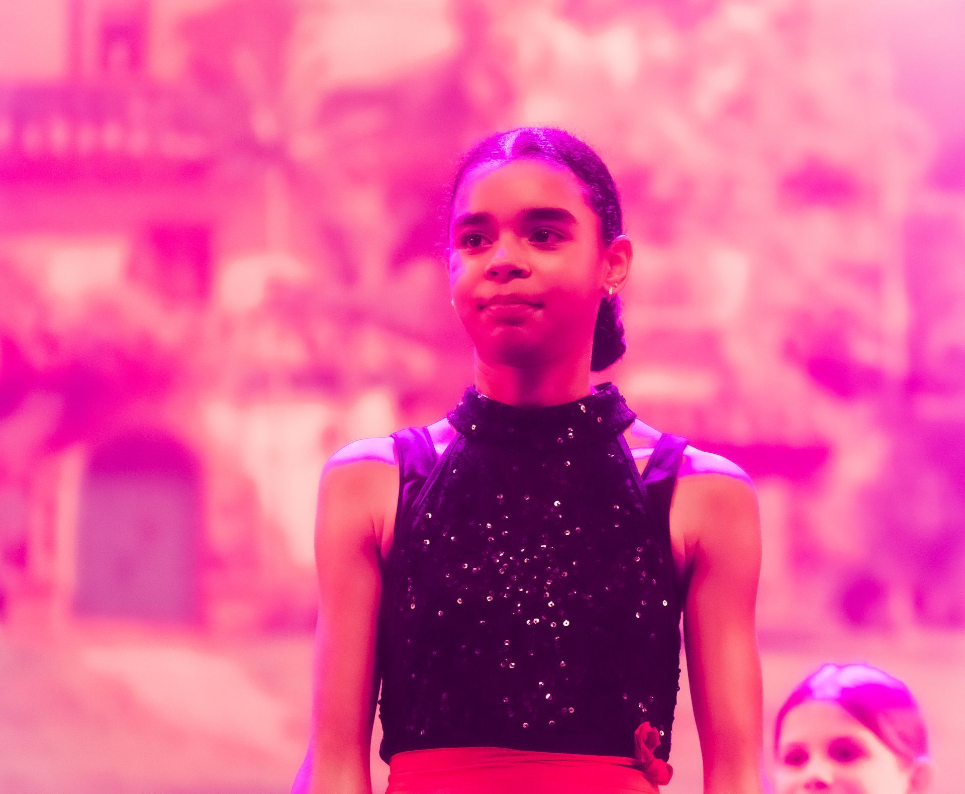 Een danseres in een zwart topje met pailletten en een rode rok treedt op een podium op met roze verlichting.