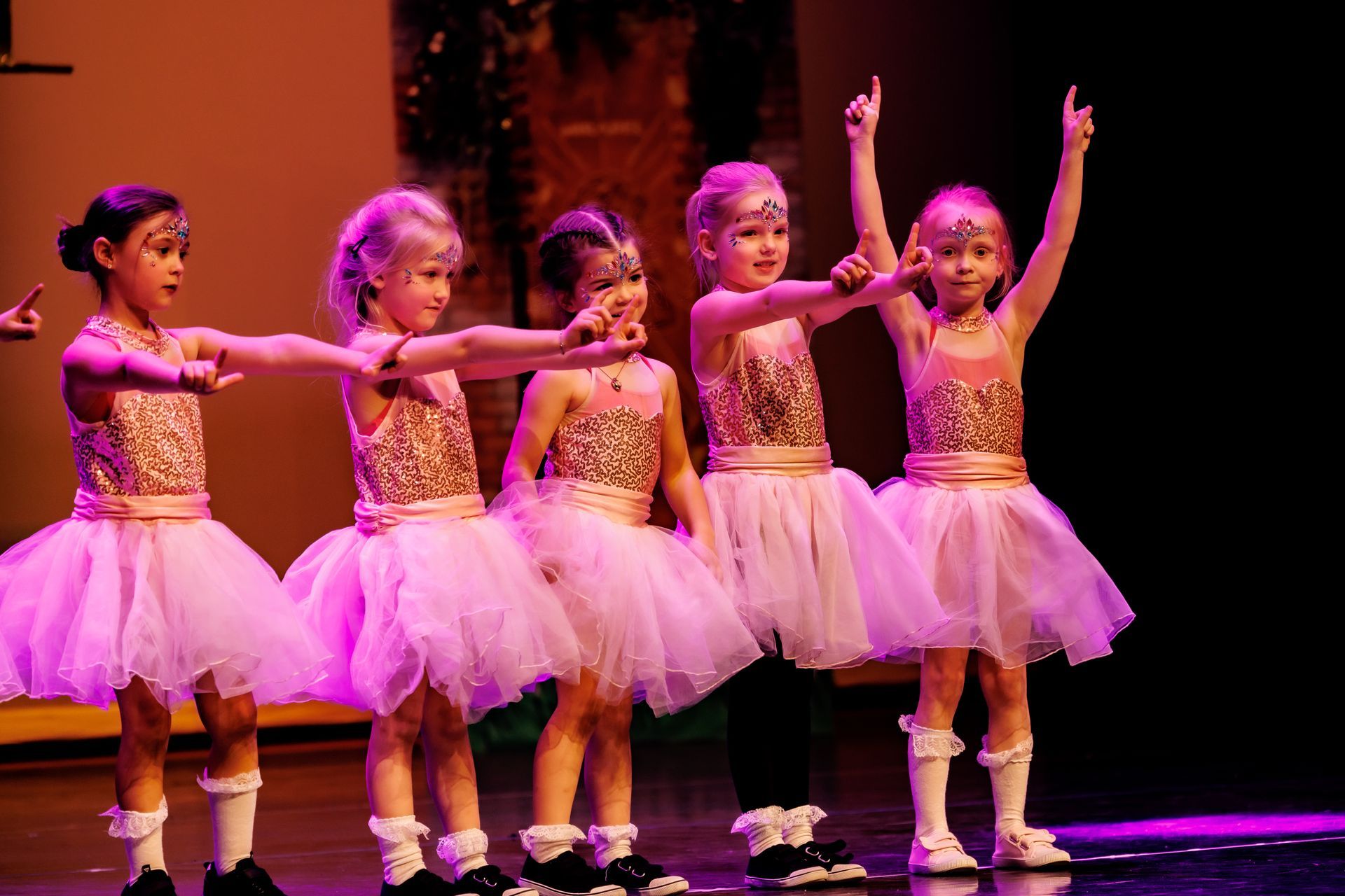 Vijf jonge danseressen in roze tutu's  treden op het podium op.