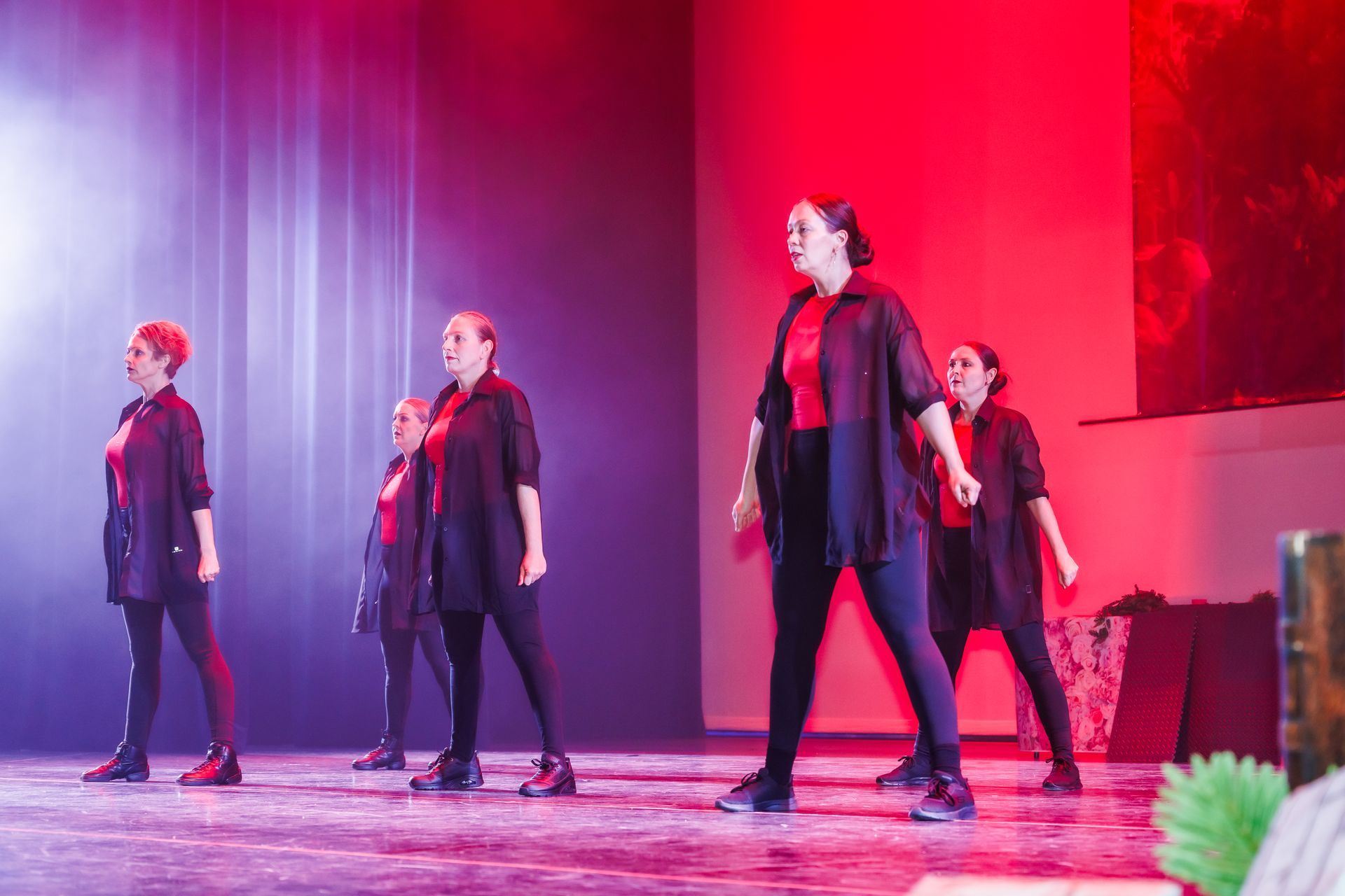 Dansers op een podium. Ze dragen zwart en rood, met rode en roze podiumverlichting.