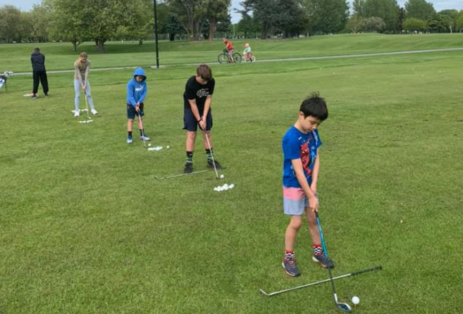 A group of children are playing golf in a park.