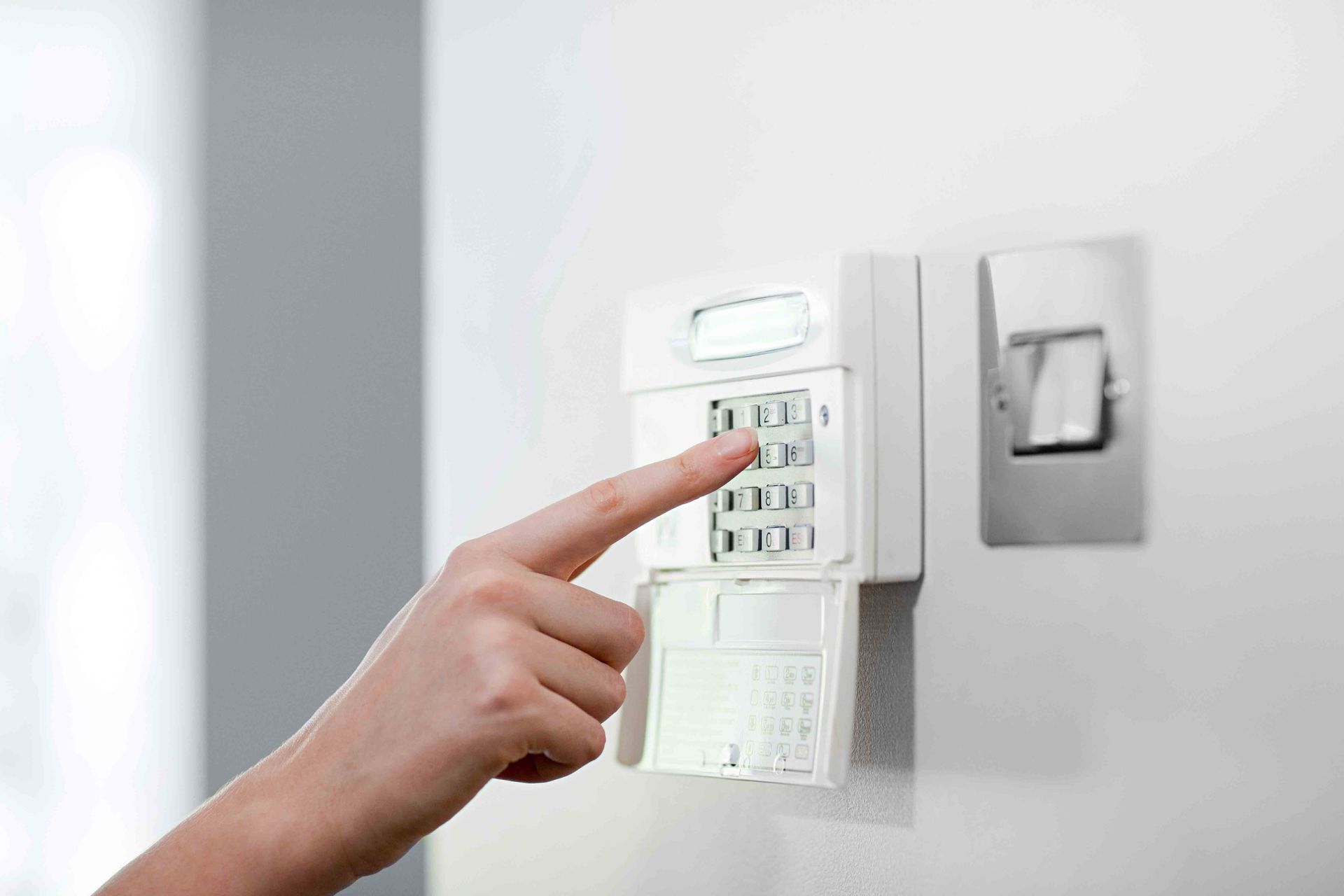 Person entering code on a wall-mounted keypad for home alarm systems security.