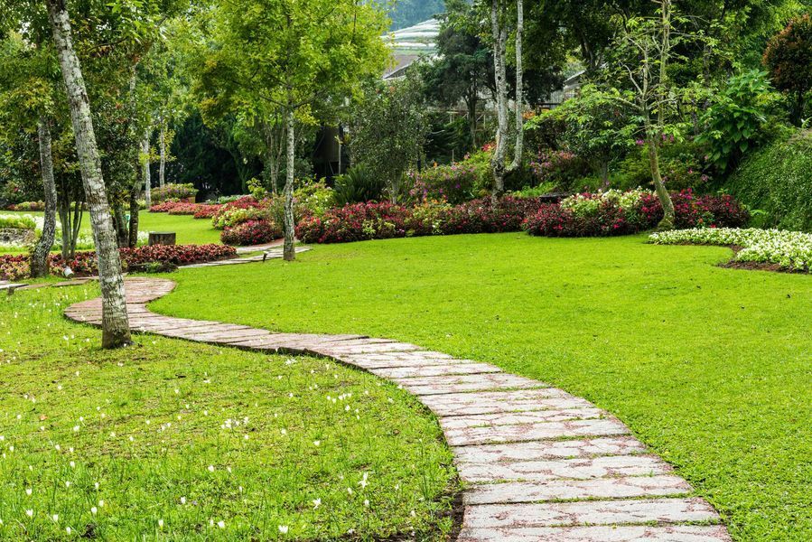 Un sentiero in pietra si snoda attraverso un rigoglioso prato verde e aiuole fiorite in un giardino.