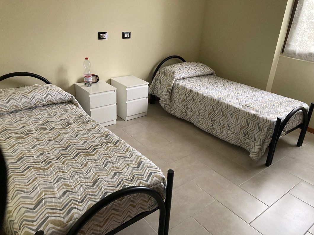 Due letti singoli con biancheria da letto a fantasia e due comodini bianchi in una stanza con pareti dai colori chiari.