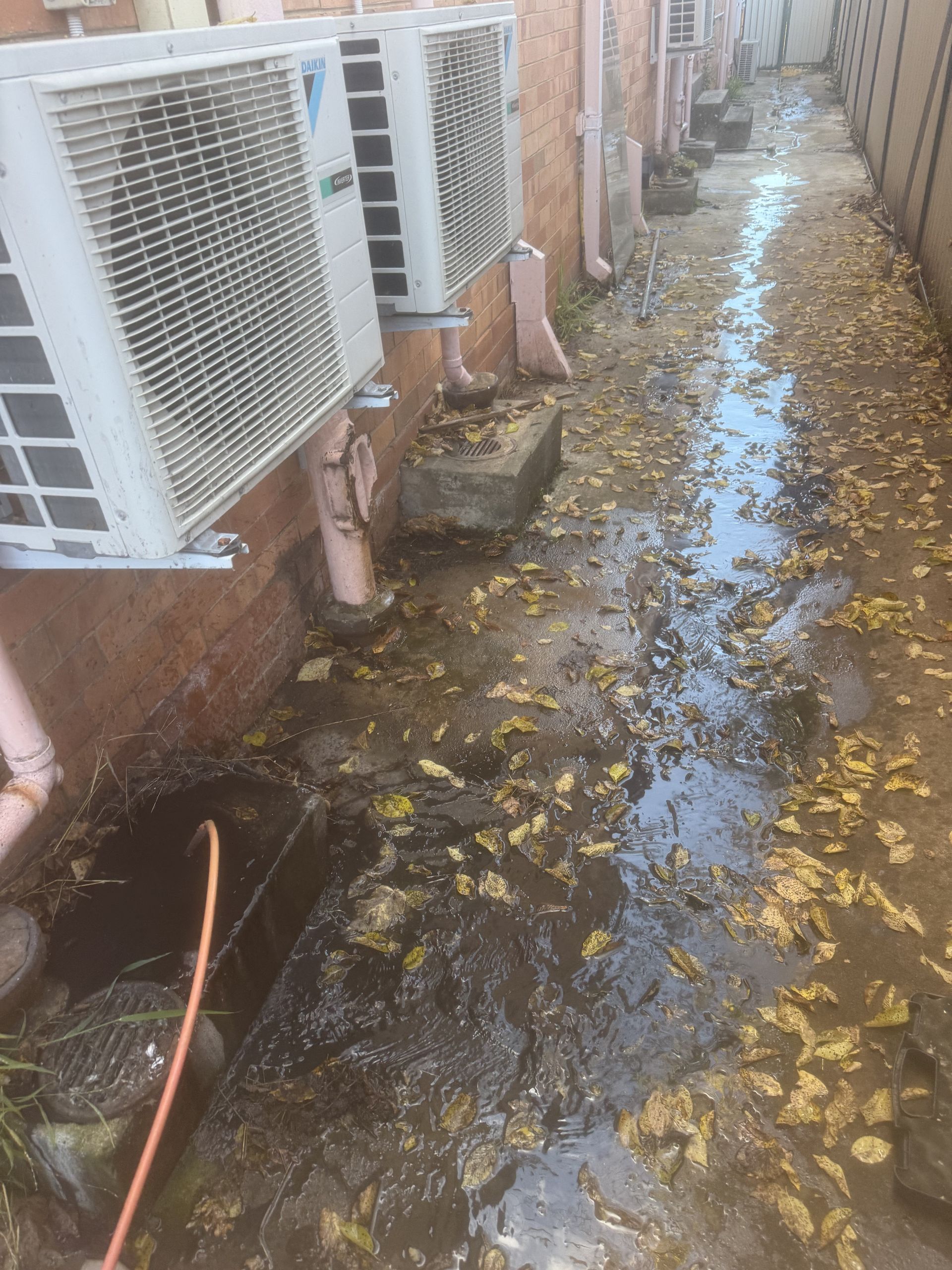 A dirty alleyway with a bunch of air conditioners on the side of a building.