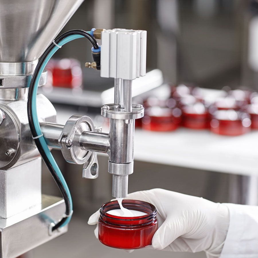 A photo of a hand filling a glass jar at a beauty cream manufacturing plant