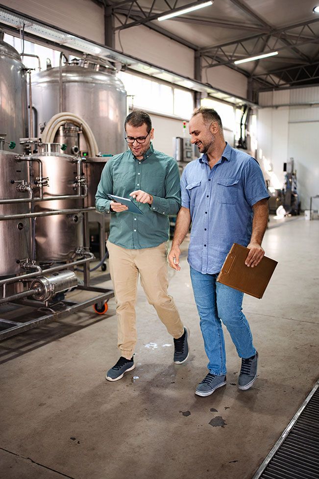 Two men walking through a brewery looking at information on a digital tablet