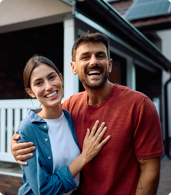 Two smiling people standing close together outdoors, one with an arm around the other