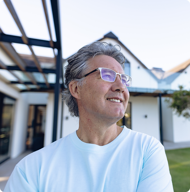 Smiling man in glasses and a white shirt standing outdoors near modern houses