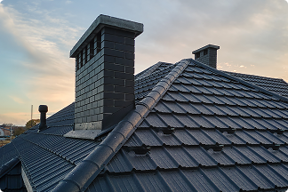 Dark gray tiled roof with two chimneys at sunset