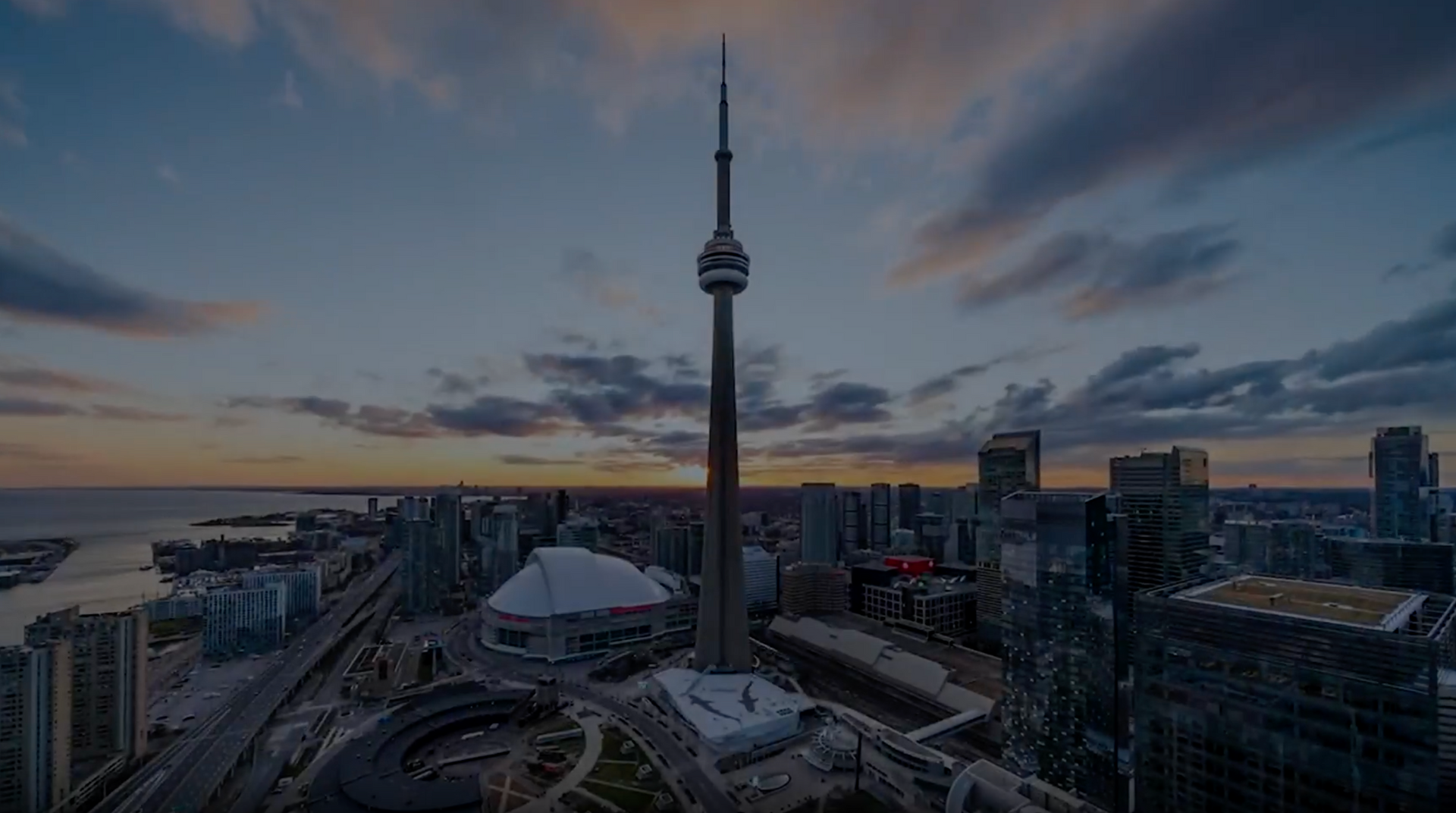 CN Tower in Toronto skyline at dusk, with buildings and highway below.