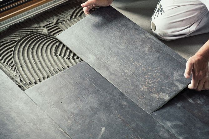 Worker laying dark floor tiles over adhesive mortar in a room under construction