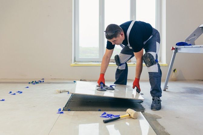 Worker installing flooring with tools in a room, kneeling over a floor opening.