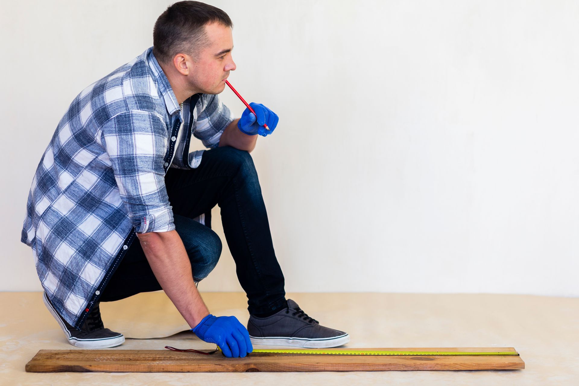 Worker kneeling on floor measuring a plank with a tape measure and wearing blue gloves