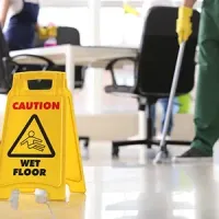 Yellow caution sign on a wet floor in a cleaning area with a mop and bucket in the background