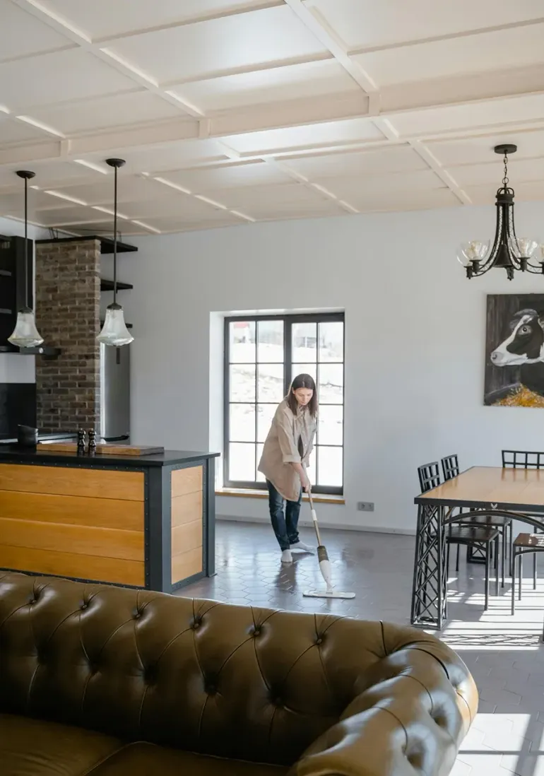 Bright café interior with a woman standing by a table, black chandelier, and tufted leather sofa in foreground