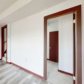 Empty white hallway with wood-trimmed doorways and gray floor tiles