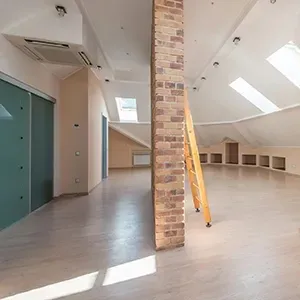 Empty loft interior with brick pillar, skylights, gray floor, and ladder near built-in cubbies