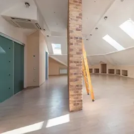 Empty attic loft with skylights, exposed brick column, and ladder leaning against the wall