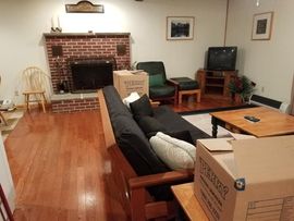 Living room with brick fireplace, sofa, TV, chairs, and wooden floors