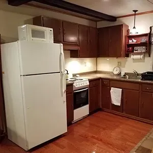 Small kitchen with white fridge, stove, wood cabinets, and hardwood floor.