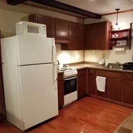 Small kitchen with white fridge, stove, wooden cabinets, and hardwood floor.