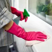 Person wearing pink gloves cleans a windowsill with a cloth and spray bottle.