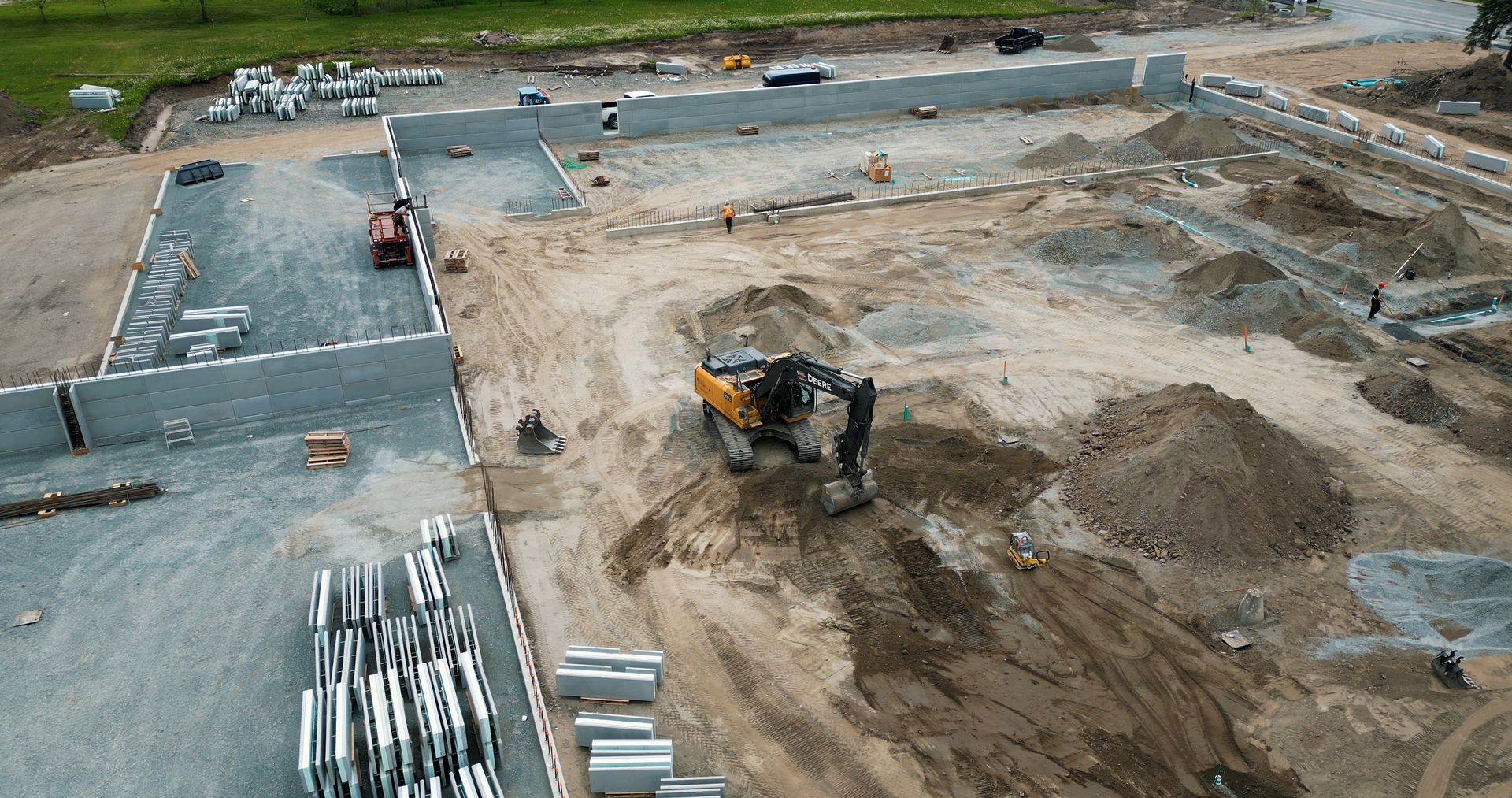Chantier de construction avec une excavatrice creusant la terre à côté d'une fondation en béton et de matériaux empilés