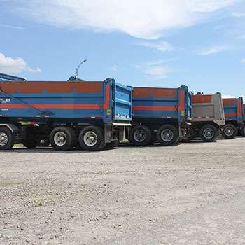 Une rangée de camions-bennes bleus et oranges garés sur un terrain de gravier sous un ciel dégagé
