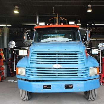 Camion bleu stationné dans un garage, vue de face avec du matériel orange à l'arrière.