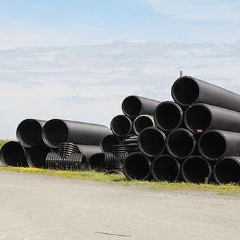 Des tuyaux de drainage noirs empilés au bord d'une route sous un ciel nuageux