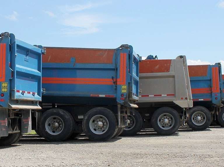Une rangée de camions-bennes bleus et orange garés sur un terrain de gravier sous un ciel dégagé