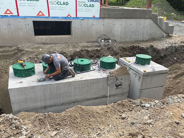 Un ouvrier s'agenouille sur des réservoirs d'eau en béton sur un chantier de construction, inspectant les plaques d'accès vertes.